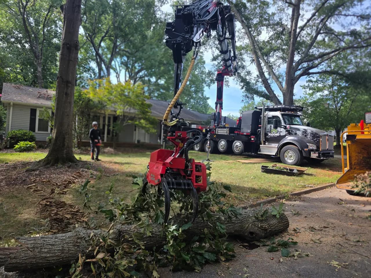 Our grapple saw truck lowering a cut trunk section into a front yard, with the chipper parked at the curb.
