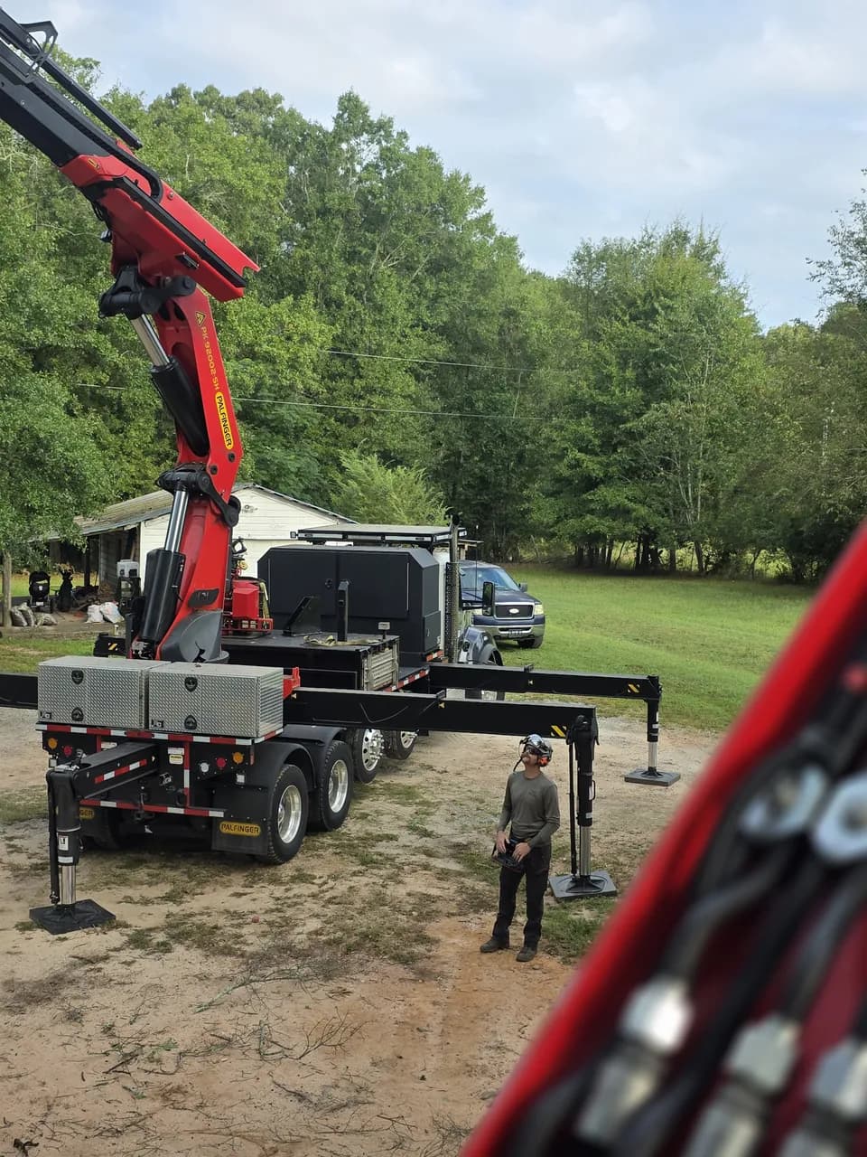 Our grapple saw crane truck set up on a rural lot with its outriggers down, a crew member standing beside it.